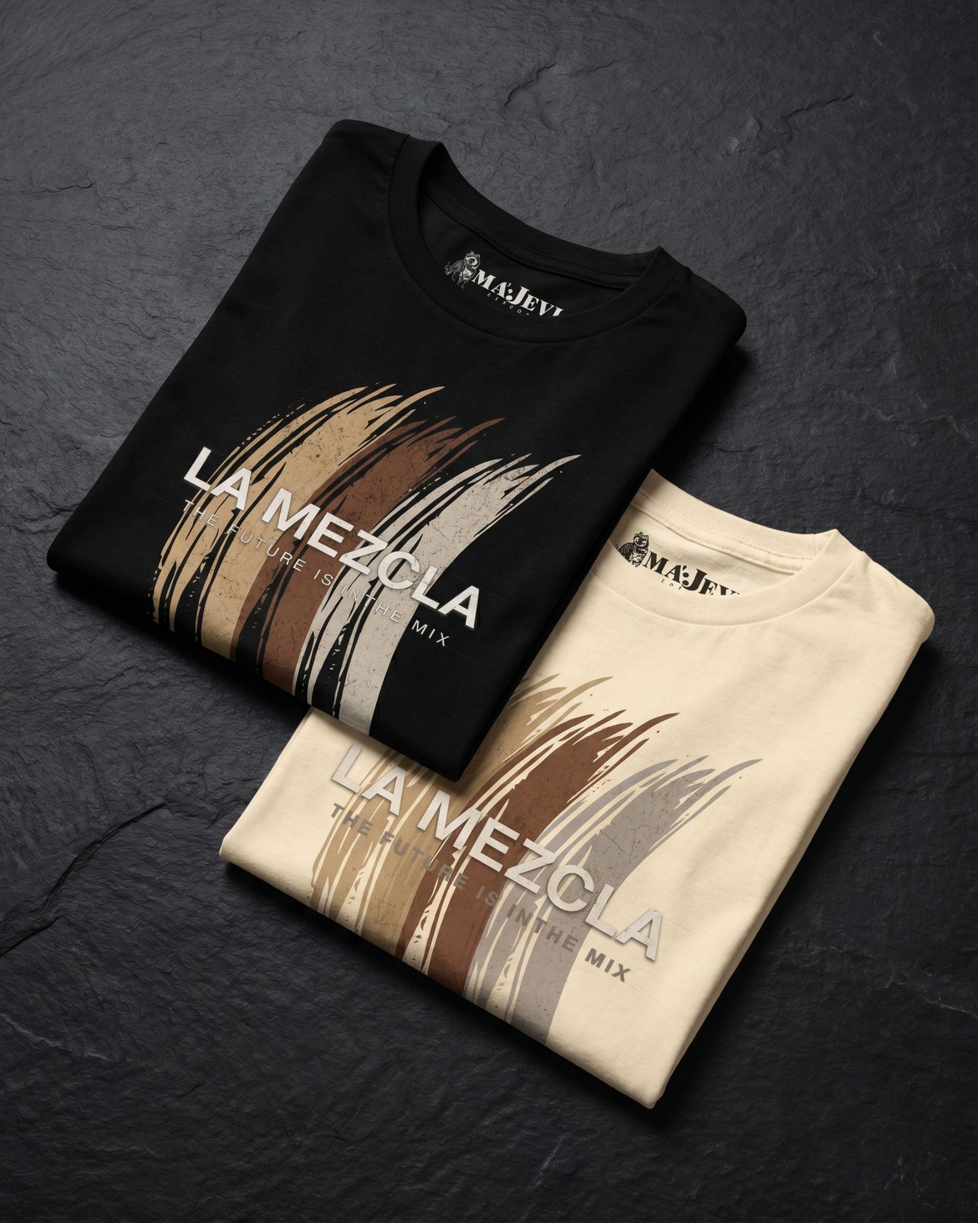 Two folded t-shirts with 'La Mezcla' design on a dark surface